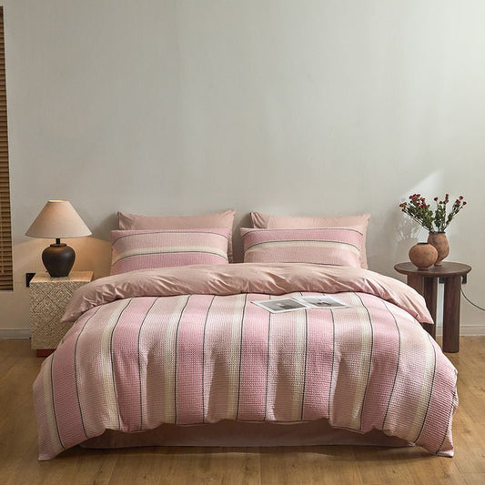 A duvet cover set with pink and white stripes on a bed, with a nightstand and a lamp beside it.