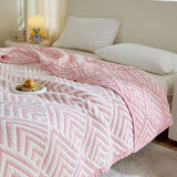 A pink and white geometric patterned blanket on a bed in a bedroom setting, with a bowl and apple on the bed, and a teddy bear and lamp in the background.