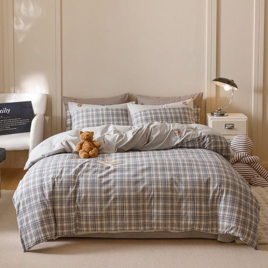 A bedding set with a grid stripe pattern displayed on a bed, with additional details such as a teddy bear, pillows, and a lamp in the room.
