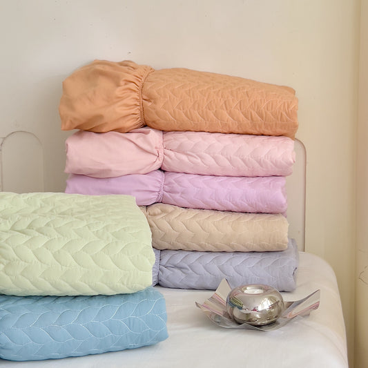 A stack of folded fitted sheets in various colors including beige, pink, blue, and green, displayed on a chair with a decorative object beside.
