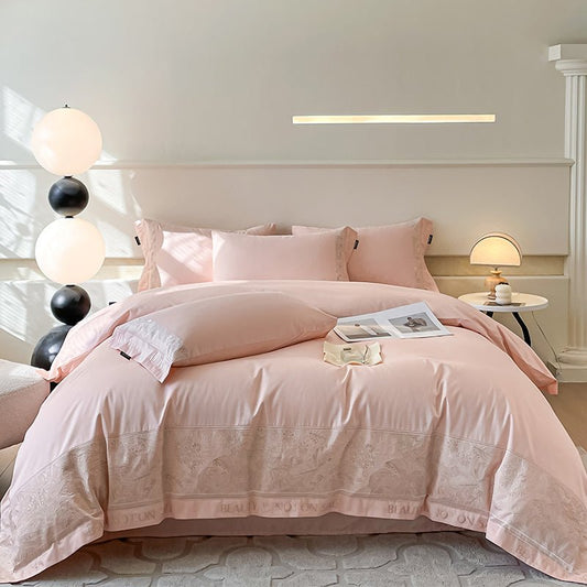 A bedding set in pink, displayed on a bed in a room with bedside tables and lamps.
