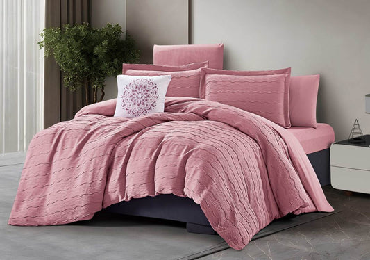 A pink comforter set on a bed, with additional pillows and a decorative pillow with a floral design in a room.
