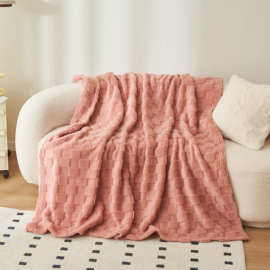 A pink weighted blanket draped over the back of a beige sofa, with a patterned rug visible beneath the sofa.