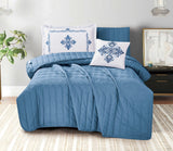 Blue quilted comforter set with decorative pillows on a bed in a bedroom setting.