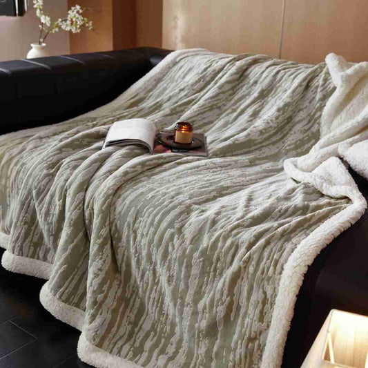 A beige Bohemian Fringe Sherpa Throw Blanket draped over the edge of a dark sofa, displaying its plush texture and fringe detailing.