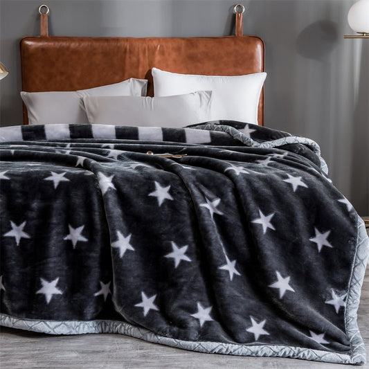 A gray and black Raschel fleece sofa blanket with star patterns, draped over a sofa with a brown leather headboard in the background.