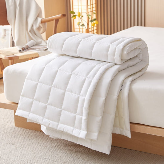 A white Stonewashed Cotton Mattress Pad rolled up and placed on a bed in a bedroom setting