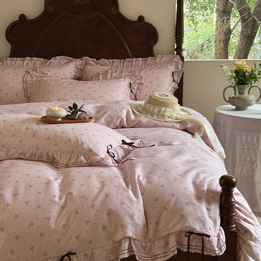 A pink floral duvet cover set on a bed, with matching pillows and bedsheet, in a room with a wooden headboard and a nightstand.