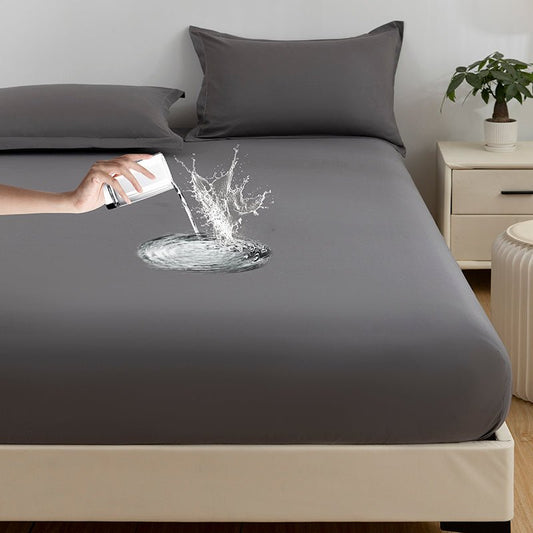 A gray fitted sheet on a bed with a person's hand sprinkling water on the sheet, showing the waterproof quality of the fabric.