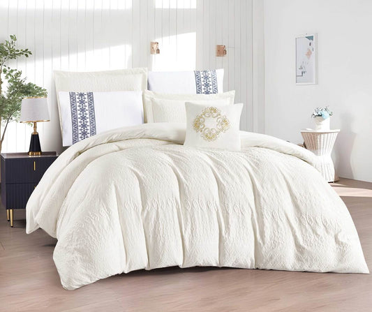 A white comforter set with shams displayed on a bed, with additional decorative pillows and a framed picture on the wall in the background.