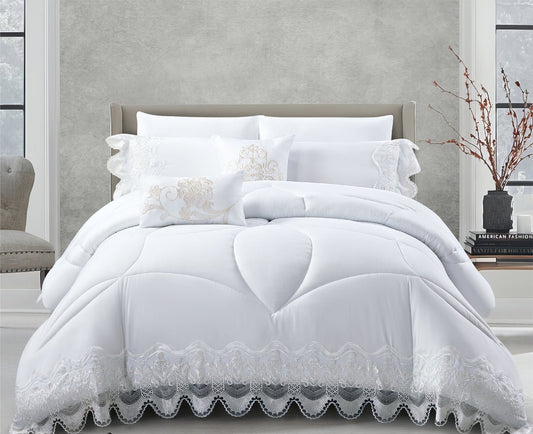 A white lace quilted comforter set on a bed, with accompanying pillows and a bedsheet, in a room with a gray wall and a branch in a vase on the side.