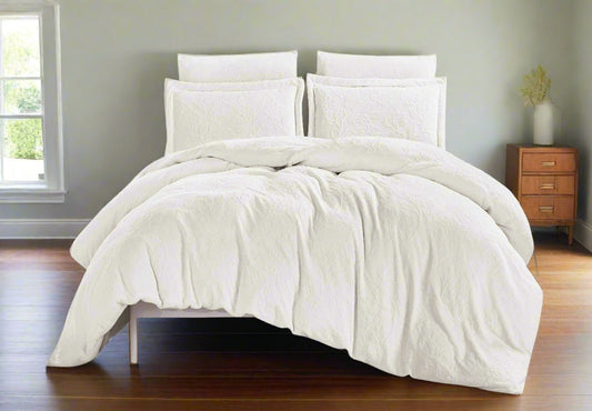 A white flannel comforter set on a bed, with a duvet cover and two pillow shams. The room setting includes a window and a wooden side table with a lamp.