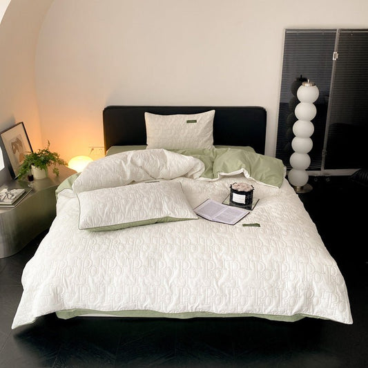 A white cotton quilted duvet cover set on a bed, with pillowcases and a book placed on top of the duvet.