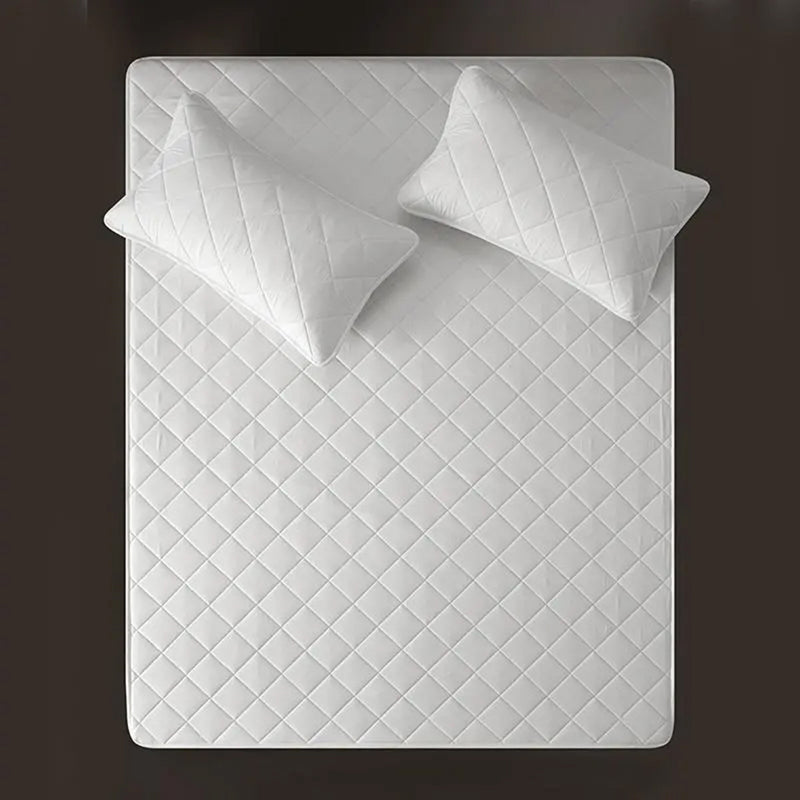 A white, waterproof mattress protector with a quilted design, displayed with two pillows on top.