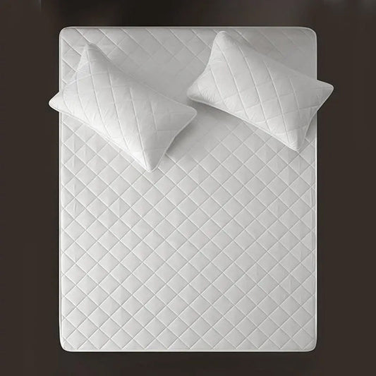 A white, waterproof mattress protector with a quilted design, displayed with two pillows on top.
