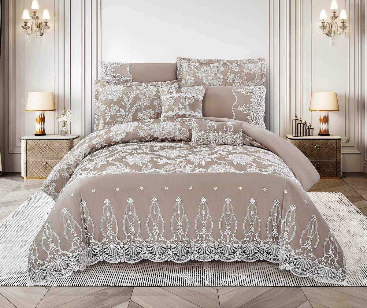 A beige and white lace comforter set on a bed, with additional pillows and decorative bedding, presented in a stylish bedroom setting.