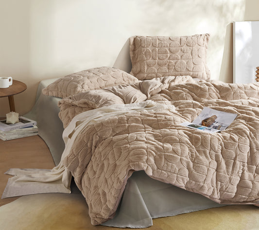 Beige textured comforter set on a bed with pillows and a side table in a bedroom setting.