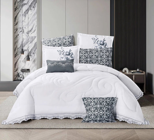 A white lace quilted bedding set with floral patterns, displayed on a bed in a room with wooden flooring and a dark grey wall in the background.