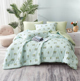 A green summer comforter set with a floral pattern displayed on a bed, accompanied by matching pillows and a book on the bed.