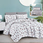 Floral bedding set on a bed with a nightstand and lamp in a room setting.