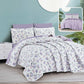 Floral bedding set with purple accents on a bed in a room with a light blue wall.