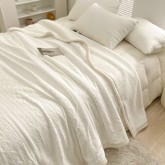 A white fleece blanket draped over a bed with pillows and a book on the surface.