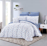 Floral bedding set on a bed in a bedroom with light blue walls and a nightstand.