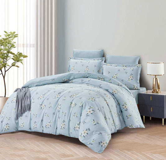 Blue floral bedding set on a bed in a bedroom with a lamp and plant.