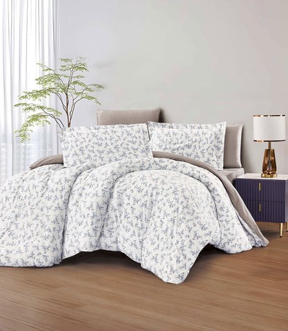Floral patterned comforter set on a bed in a bedroom setting with a lamp and plant.