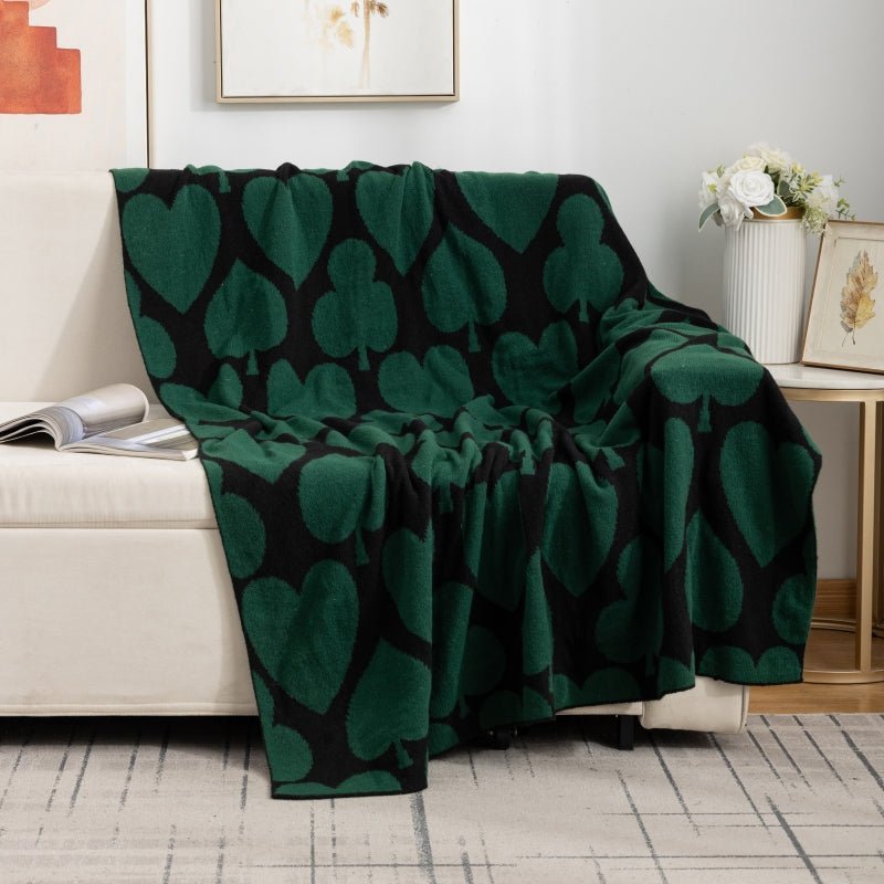 A green geometric patterned blanket thrown over the back of a beige sofa in a living room setting.