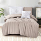 Beige quilted comforter set on a bed in a bedroom setting with pillows and a plant.