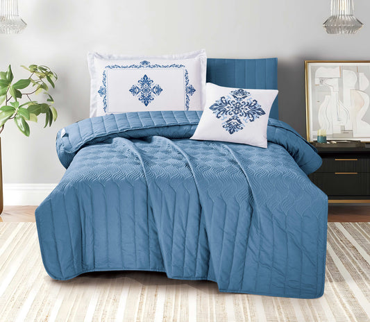 Blue quilted comforter set with decorative pillows on a bed in a bedroom setting.