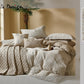 Neatly made bed with textured bedding and pillows in a room with a window and plant.